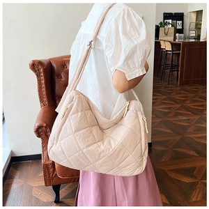 Detailed side view of a beige quilted puffer tote bag with wide shoulder strap