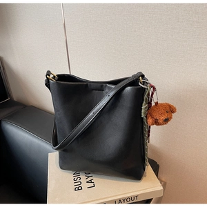 Detail of black leather bucket bag featuring a plush bear charm and woven rope accent