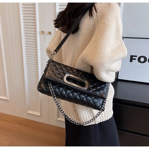 Detail einer schwarzen gesteppten Ledertasche mit Silberkette und Metallgriff am Modell