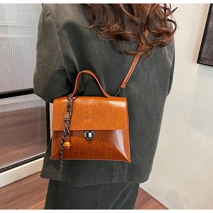 Detail der braunen Vintage-Lederhandtasche mit Metallglocke und geflochtenem Anhänger