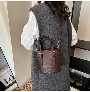 Brown litchi grain leather bucket bag shown as a crossbody on model's shoulder