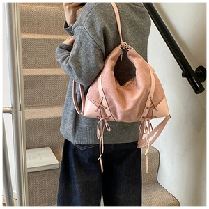 Detailed side view of pink suede shoulder bag with decorative crisscross woven straps