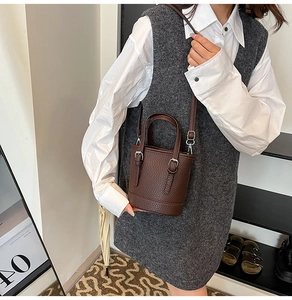 Close-up of brown litchi leather bucket bag with metal buckle straps on a model