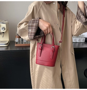 Close-up of red lychee textured mini bucket bag with silver metal buckles on street style