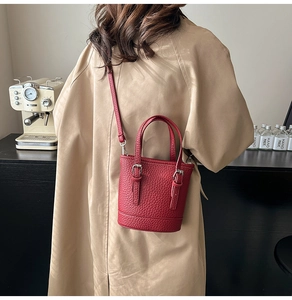 Close-up of deep red pebble leather bucket bag with silver buckles worn as a crossbody