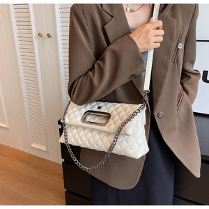 Details einer weißen Stepptasche mit silberner Kette und Metallgriff an einem Modell