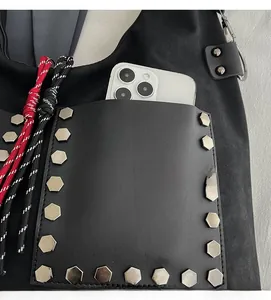 Detail of black tote bag front pocket with silver rivets showing smartphone storage