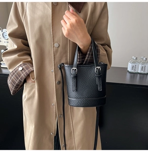 Detail of black pebbled leather bucket bag featuring metal buckle and crossbody strap