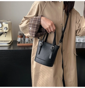 Close-up of black lychee grain bucket bag with leather handle and metallic buckle detail