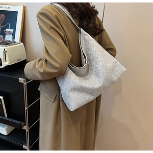 Détail d'un sac cabas gris argenté orné de strass porté sur un trench-coat beige