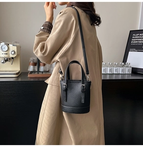 Detail shot of black litchi textured bucket bag worn with a stylish khaki trench coat