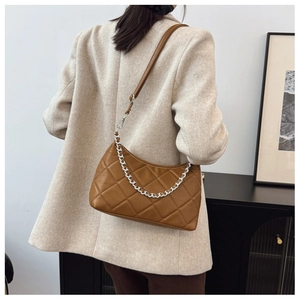 Side view of a brown quilted shoulder bag with chain detail on a beige blazer