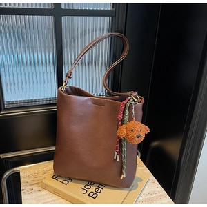 Detail of coffee brown tote bag with woven pendants and a plush dog charm on a marble base