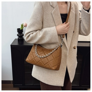 Detailed view of brown quilted handbag with silver chain on model in home setting