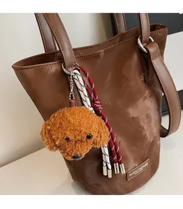 Detail of plush poodle bag charm with woven rope and metal chain on a brown handbag