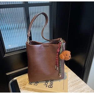 Detail of dark brown leather bucket bag with a plush teddy bear charm and braided ropes