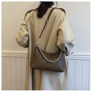 Detailed view of brown quilted hobo bag with silver chain and adjustable strap on a beige coat