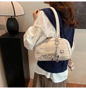 Détail du sac sous le bras crème avec nœuds en ruban et pendentif cœur argenté