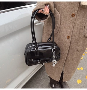 Détail du sac sous le bras en cuir verni noir avec charme d'ours argenté et nœud