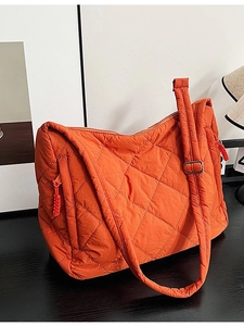 Orange quilted tote bag with diamond pattern and adjustable strap on a wooden table
