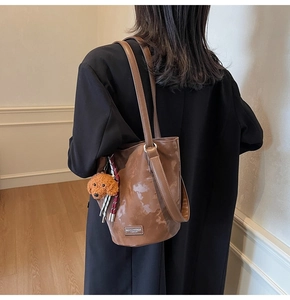 Brown glossy shoulder bag featuring a cute teddy dog plush charm and logo plate detail