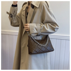 Detail of dark brown quilted crossbody bag with silver chain worn on a beige coat