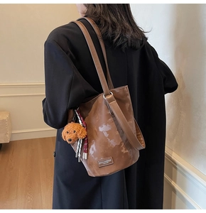 Brown leather bucket bag with a cute teddy bear charm shown on model in a modern interior