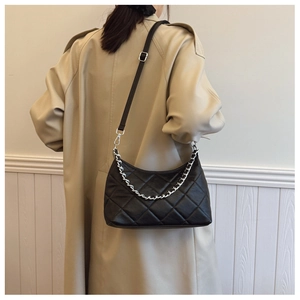 Side view of black quilted crossbody bag with silver chain strap on a trench coat