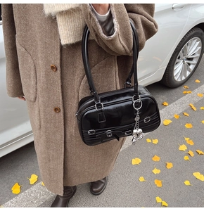 Détail du sac à main noir brillant avec nœud et pendentifs métalliques argentés