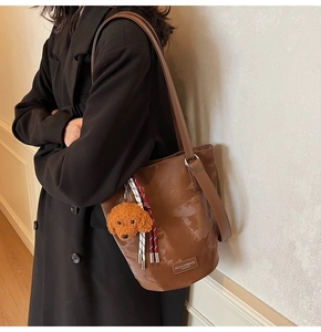 Detail of a brown leather bucket bag with a plush teddy charm and woven rope accent