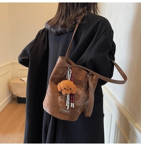 Detail of dark brown leather bucket bag with cute plush dog pendant and woven strap