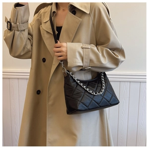 Close-up of a black quilted shoulder bag with silver chain strap worn with a beige coat
