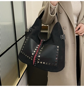 Close-up of black suede tote bag featuring silver hexagonal rivets and woven pendant detail