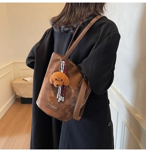 Detail of vintage brown bucket bag with plush puppy charm and striped tassel accessory
