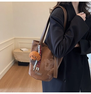 Detail of vintage brown bucket bag with plush dog charm and woven tassel details