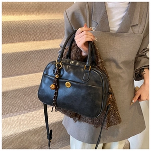 Detail of black matte Boston bag with golden buckle pocket and decorative bell charm