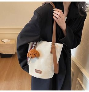 Detail of white bucket bag with brown leather strap and teddy bear charm on black blazer