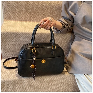 Close-up of black Boston bag with gold hardware and beaded decorative pendant charm