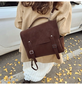 Detalle de bolso mensajero marrón oscuro mate con hebillas en un entorno otoñal