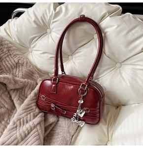 Détail du sac à main en cuir verni bordeaux avec nœud et pendentif en cœur