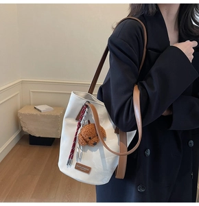 Detail of white leather bucket bag featuring a plush teddy bear charm and woven rope