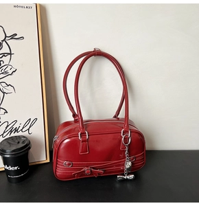 Détail d'un sac baguette rouge foncé brillant avec breloque cœur et boucle à nœud