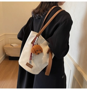 Detail of cream leather tote bag with brown straps and a teddy bear charm on model