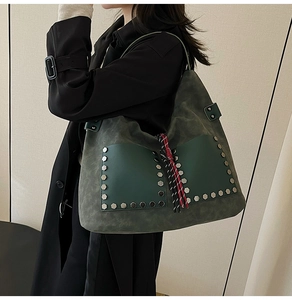 Detail of dark green suede tote bag featuring silver studs and colorful tassel accessory
