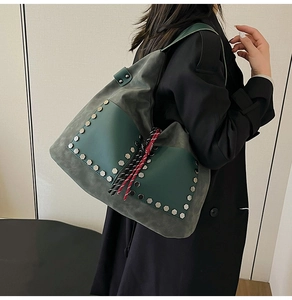Detail of dark grey-green suede bucket bag with silver hexagonal rivets and woven charm