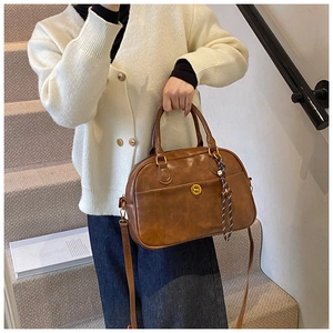 Brown leather tote bag featuring a vintage metal button pocket and adjustable shoulder strap