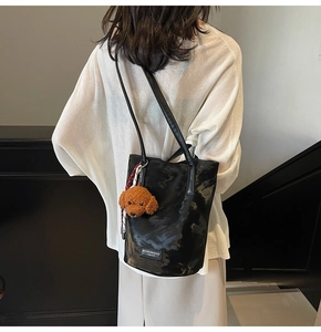Back view of a black glossy leather shoulder bag with a cute brown plush puppy charm