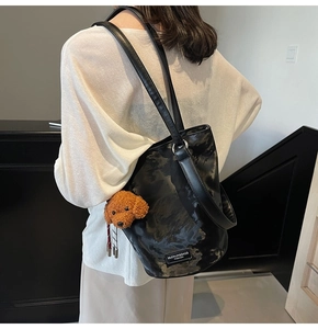 Detail of a vintage black textured bucket bag with a cute plush dog charm on the shoulder