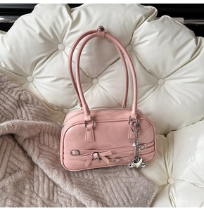 Détail du sac sous le bras en similicuir rose avec nœud et pendentif cœur argenté
