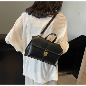 Detail of black vintage crossbody bag with white stitching and gold buckle on a model